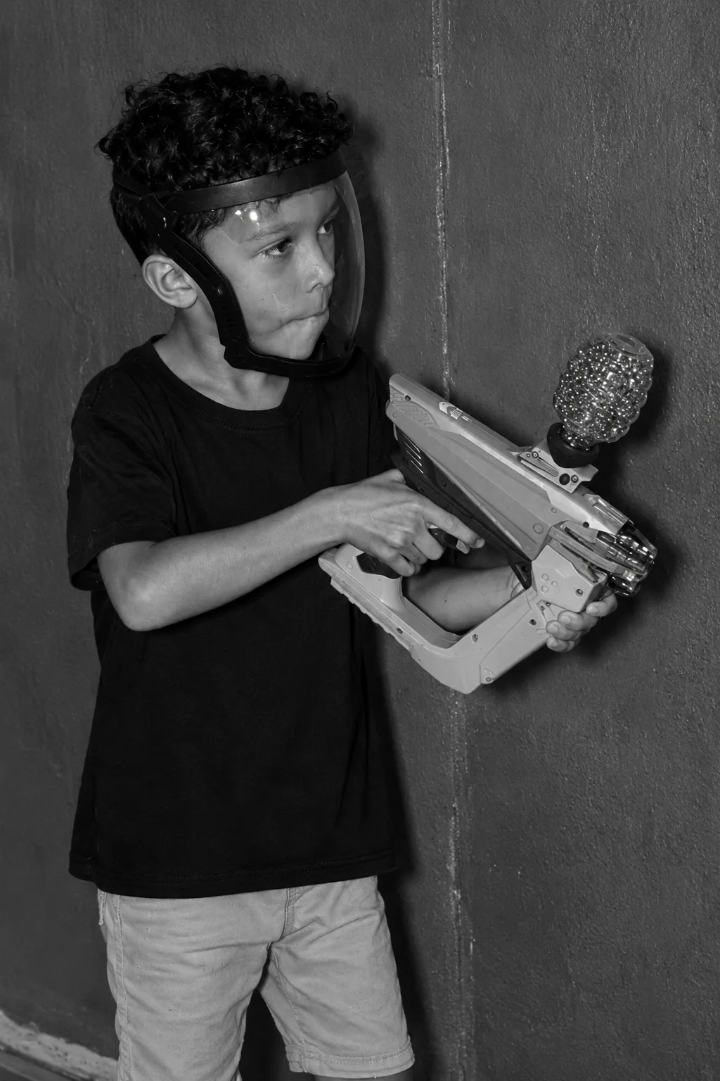 Menino com visor de proteção segurando o blaster encostado na parede